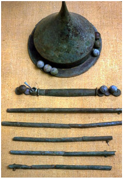 Piikkiön pronssinen, piikkilakkinen kilvenkupura ja sen yhteydessä löydetty kädensijan pronssihela (kuvassa kupuran alapuolella). Vanhempi roomalaisaika. © HY/Kulttuurien tutkimuksen laitos, Arkeologian oppiaine.